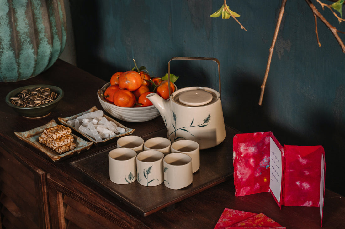 porcelain tea cups and pitcher on wooden table with fruit, cards and flowers also on the table