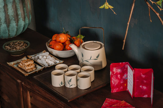 porcelain tea cups and pitcher on wooden table with fruit, cards and flowers also on the table