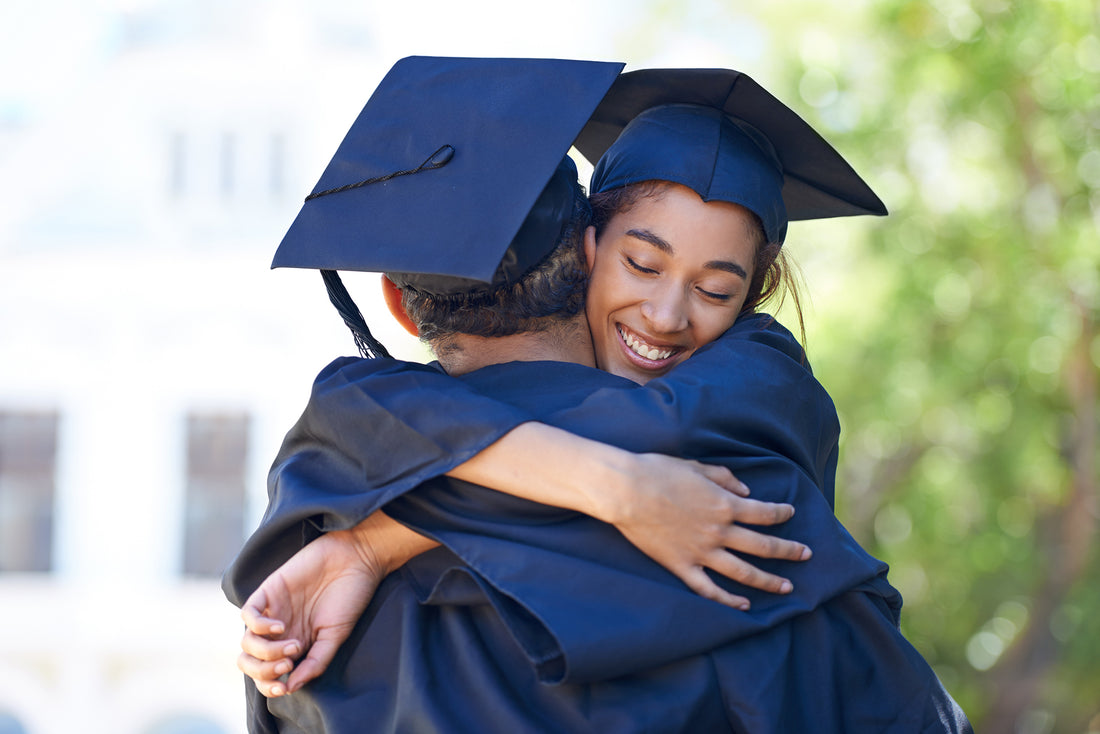 Two graduates in grad robe and hat, embracing 