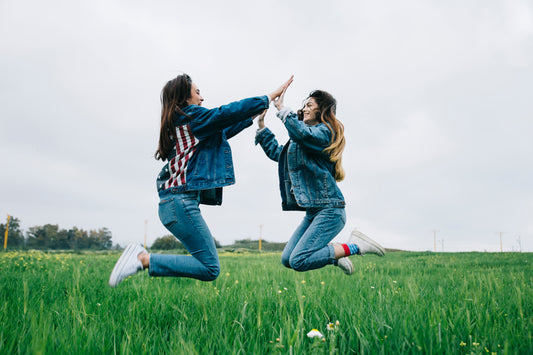 two girls jumping in the air over field of tall green grass