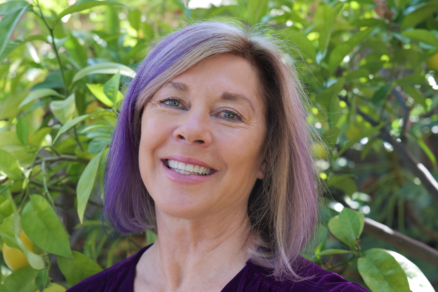 Karen Chelini with purple and grey hair and trees in the background